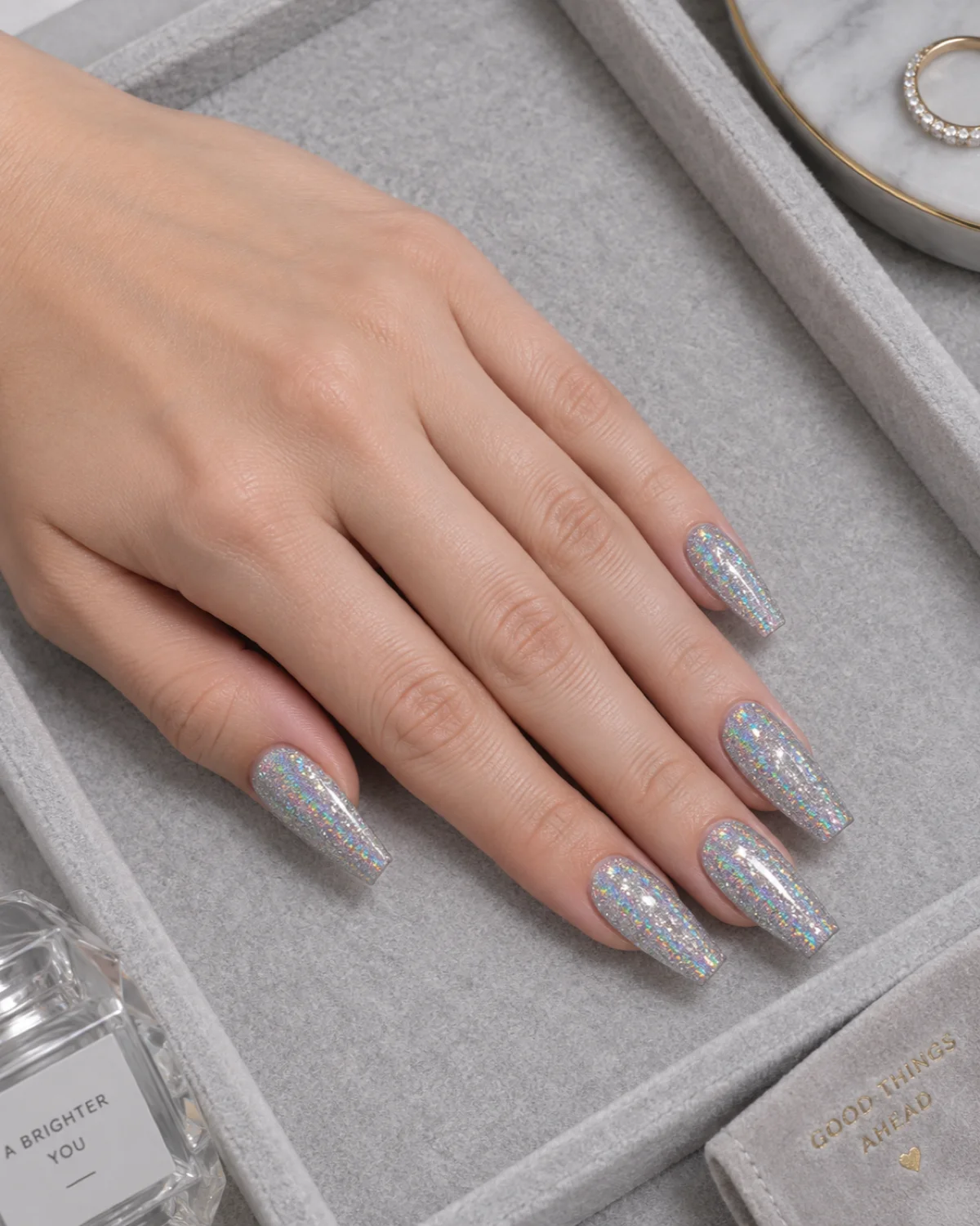 Single left hand with fine holographic silver glitter on ballerina nails on a gray felt jewelry tray