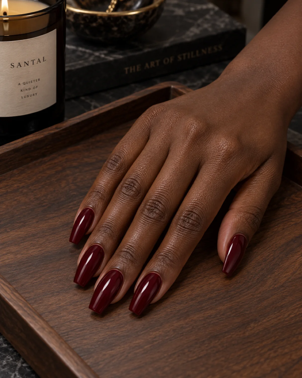 Single right hand with rich burgundy-wine polish on ballerina nails resting on a dark walnut tray