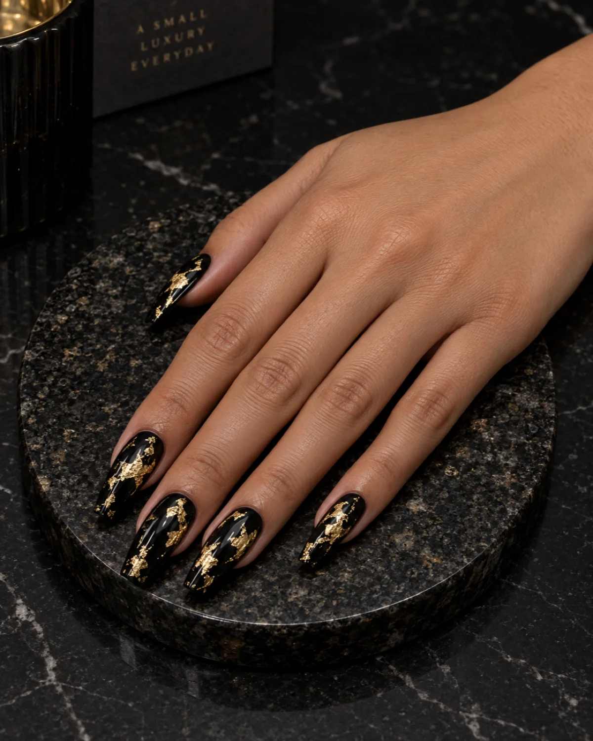 Single right hand with jet-black polish and gold-foil flakes on ballerina nails on a black granite coaster