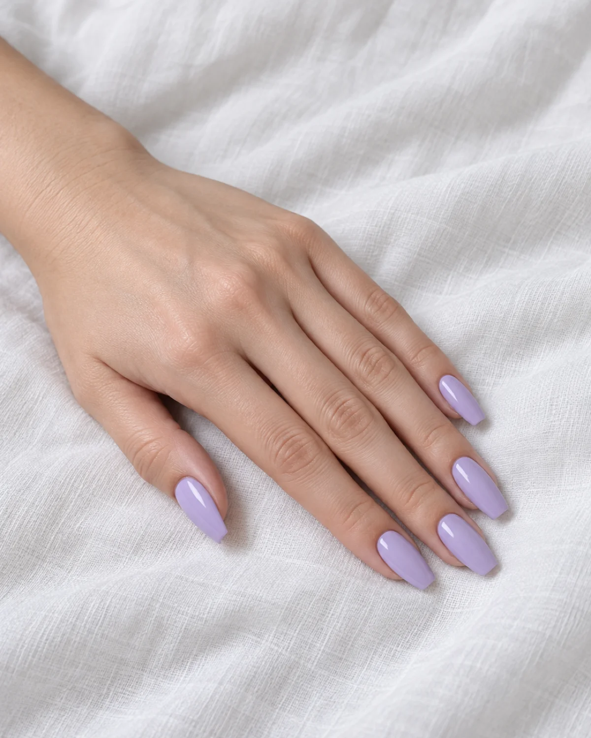 Single left hand with soft lavender-purple polish on ballerina nails resting on a white cotton cloth