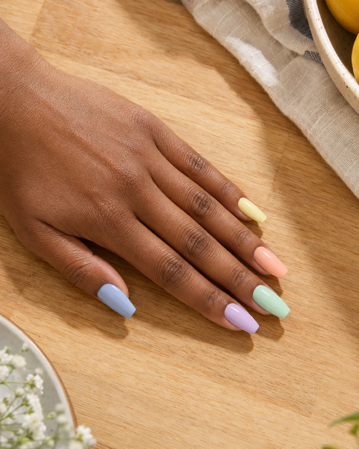 Single left hand with five different pastel-colored nails on ballerina shape on a cream terrazzo surface