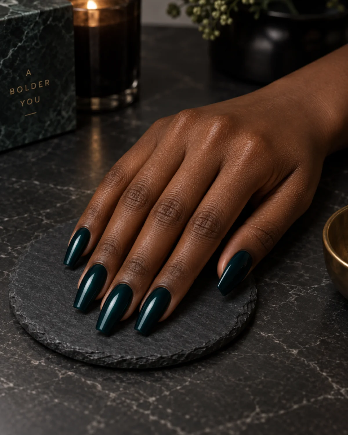 Single right hand with rich deep teal-green polish on ballerina nails resting on a dark slate coaster