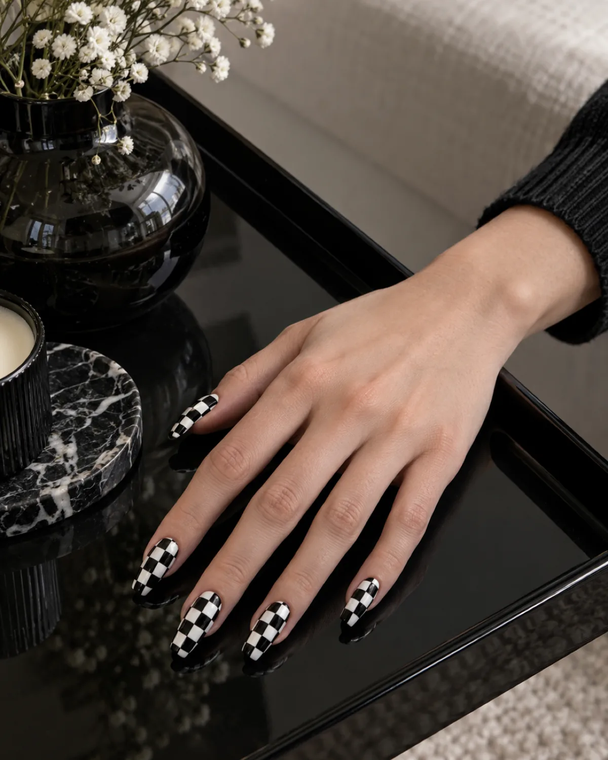 Single right hand with glossy black-and-white checkerboard coffin nails resting on a black lacquer tray