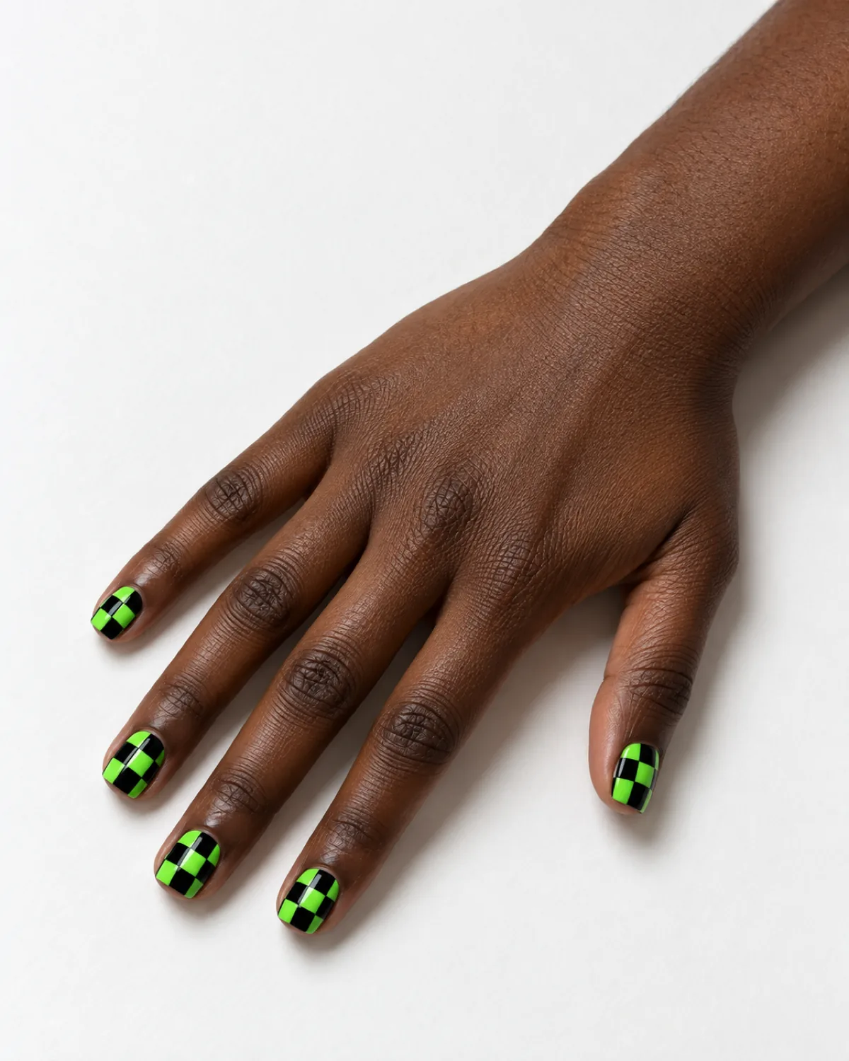 Single right hand with neon green and black checkerboard short square nails on a white surface
