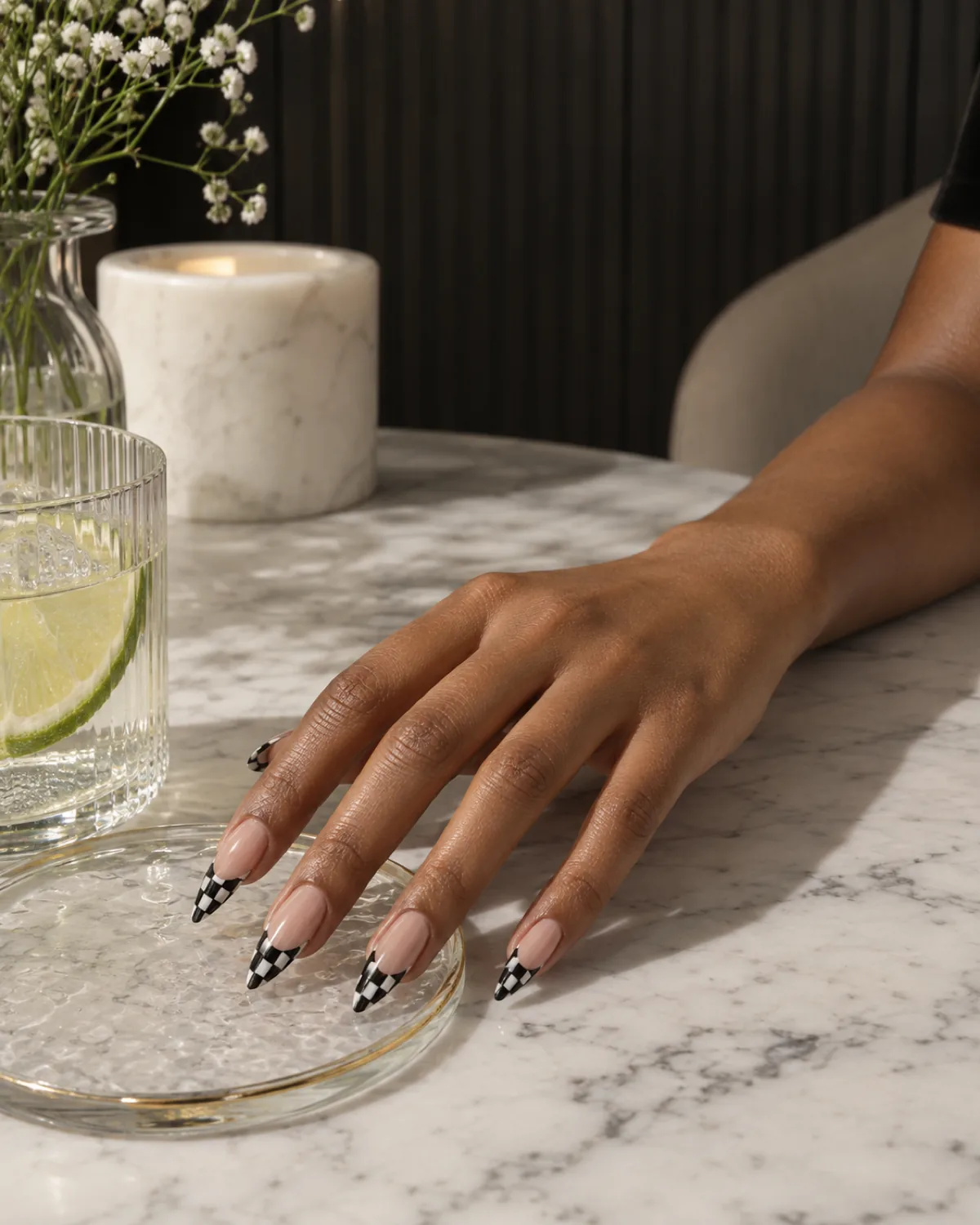 Single right hand with checkered French tips on stiletto nails resting on a clear glass coaster edge