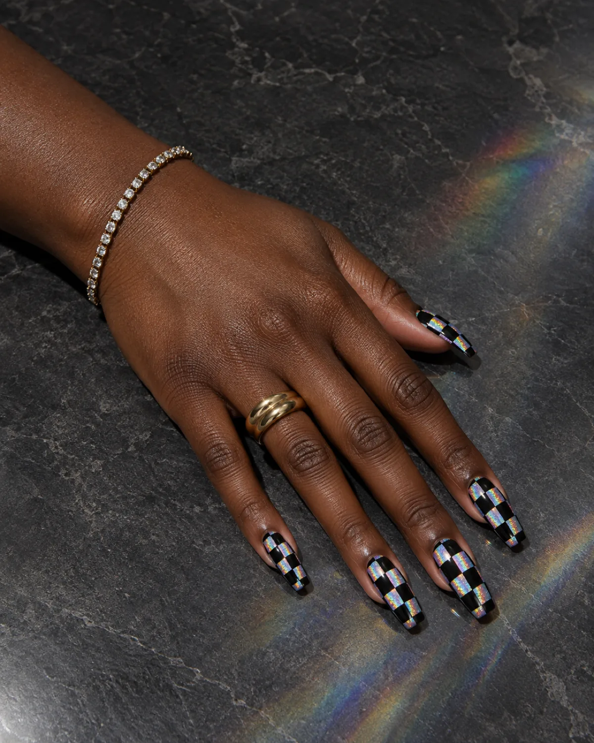 Single left hand with holographic silver and matte black checkerboard coffin nails on a dark grey stone slab