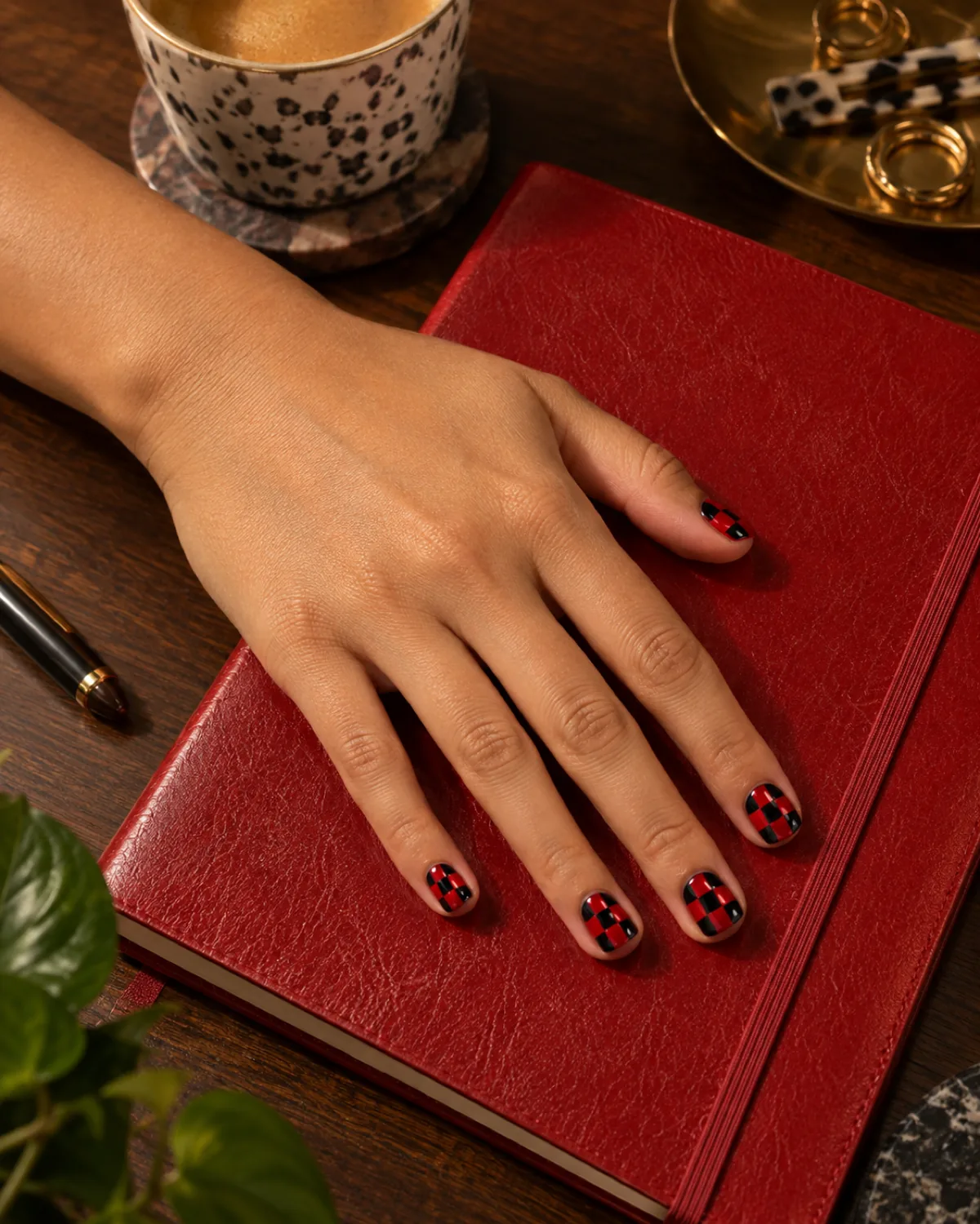Single left hand with red and black checkerboard short natural nails on a red leather notebook