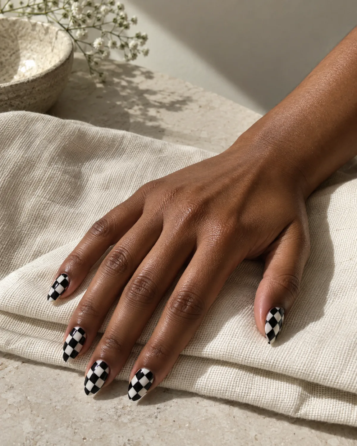Single right hand with black-and-white diagonal checkerboard almond nails on a cream cotton cloth