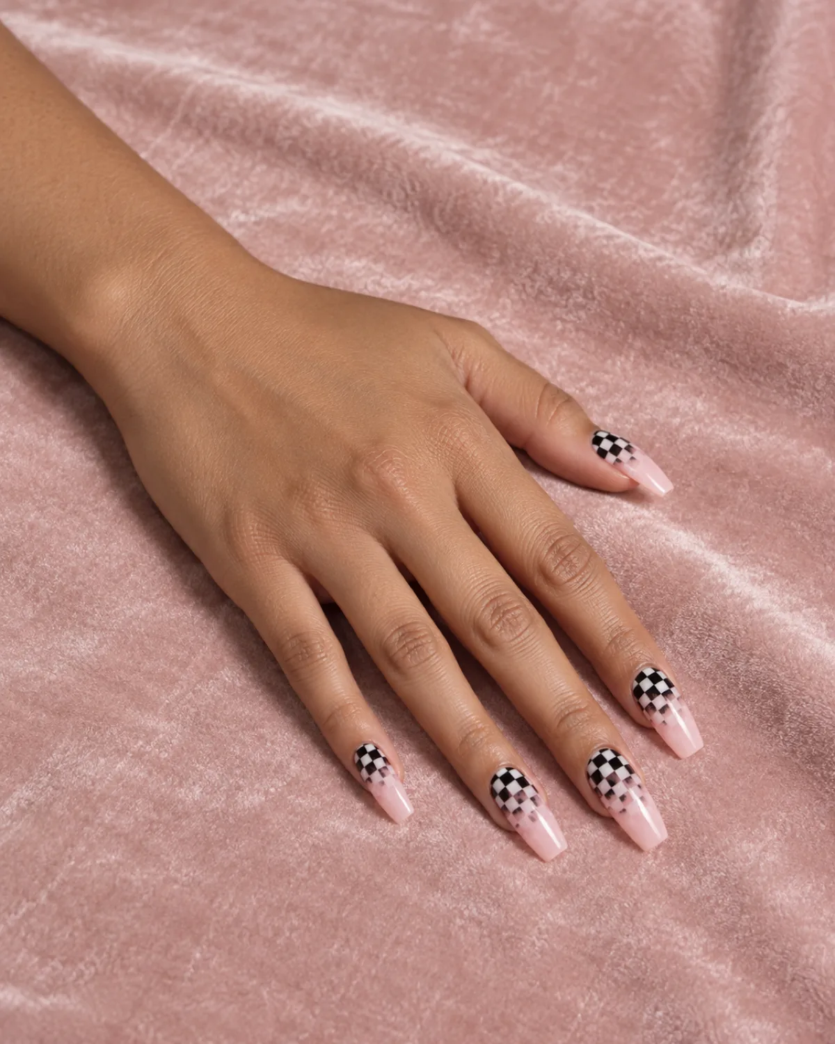Single left hand with checkered gradient fading from black-and-white at cuticle to sheer pink at tip on coffin nails on pink velvet