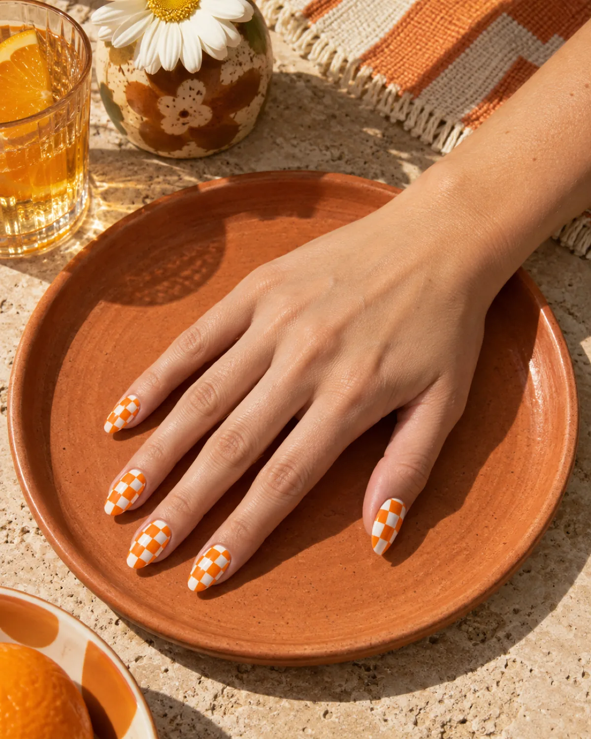 Single right hand with bright orange and white checkered almond nails on a terracotta saucer