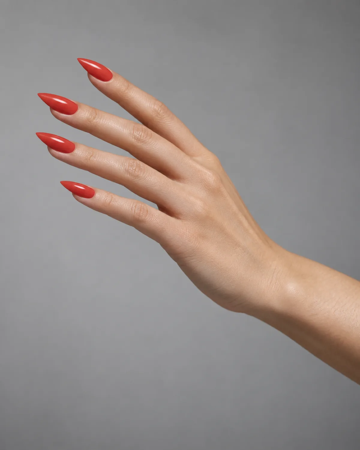 Side profile of single right hand with stiletto nails in deep reddish coral glossy crème against neutral grey backdrop