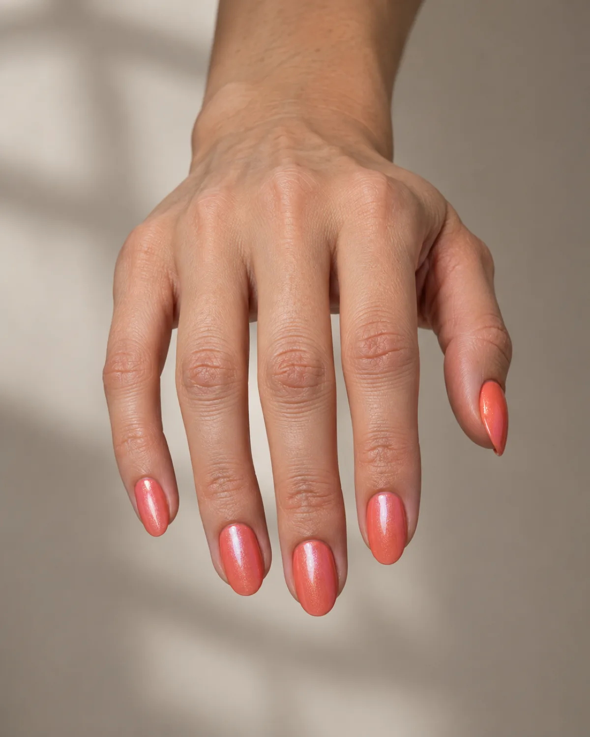 Single right hand with medium oval nails in shimmery pearl coral polish reaching down into frame from the top