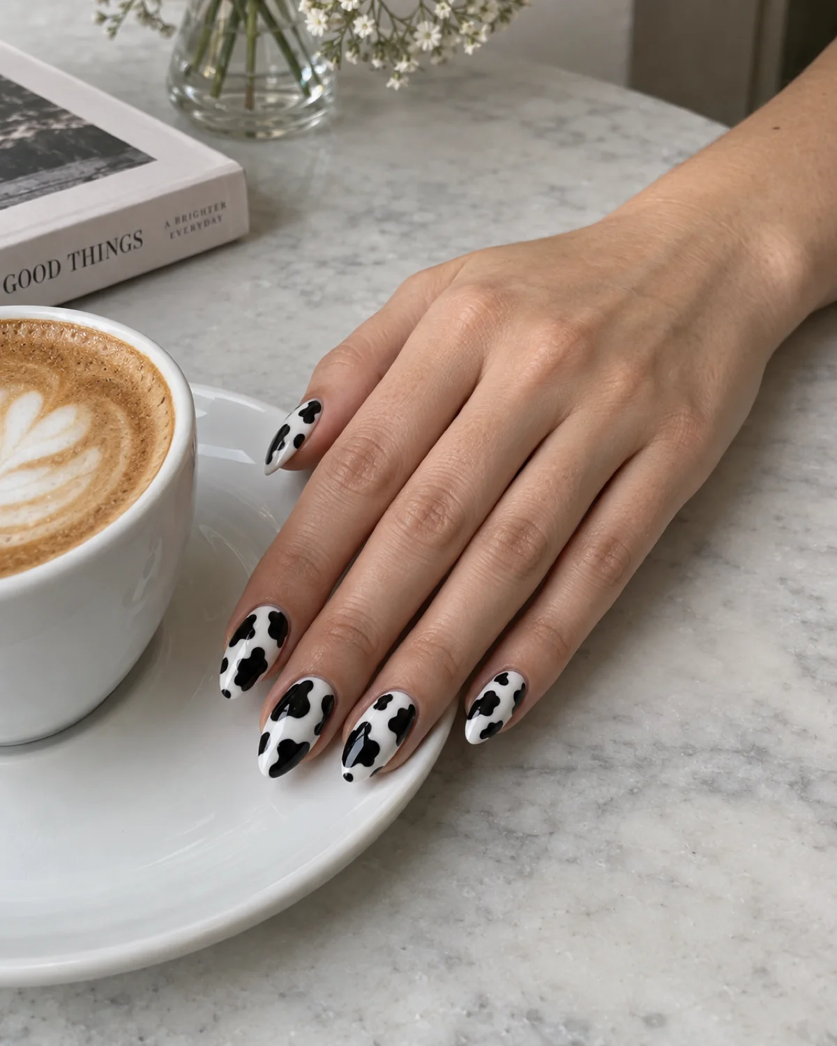 Single right hand with classic black-and-white cow print nails on almond shape resting on a white porcelain saucer