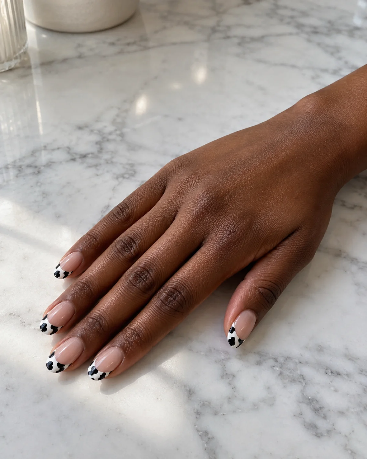 Single right hand with cow print French tip nails on oval shape resting on a white marble vanity surface