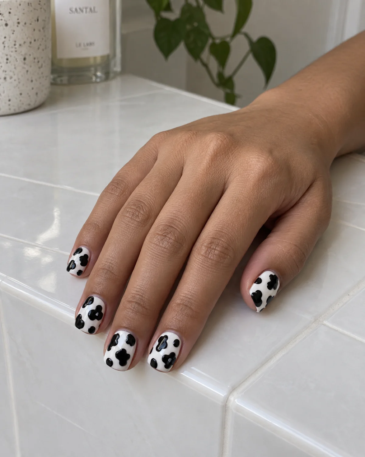 Single left hand with 3D textured black cow print nails on short square shape resting on a smooth white tile surface