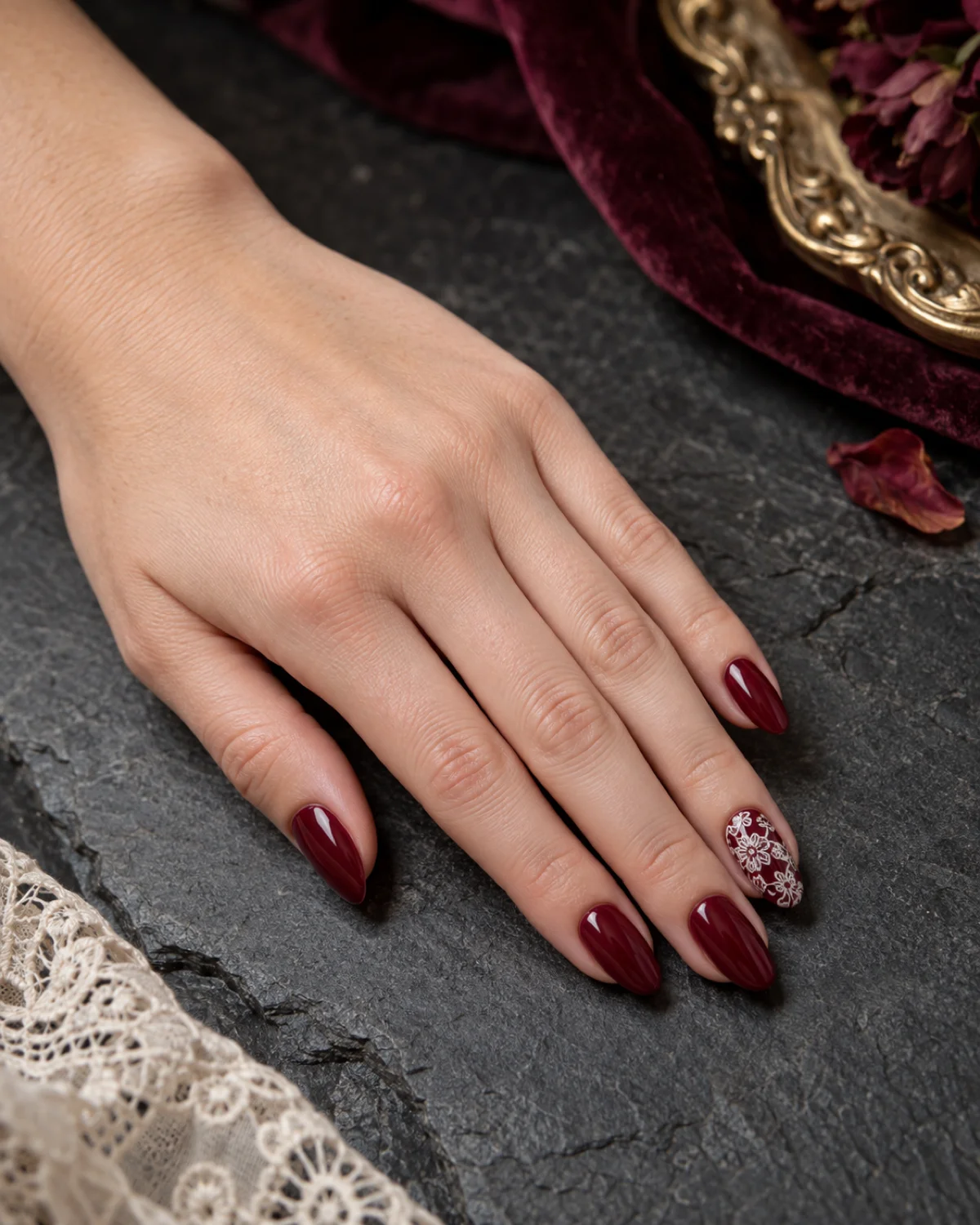 Single left hand with deep wine elegant nails and Venetian lace accent on medium almond shape resting on dark grey slate