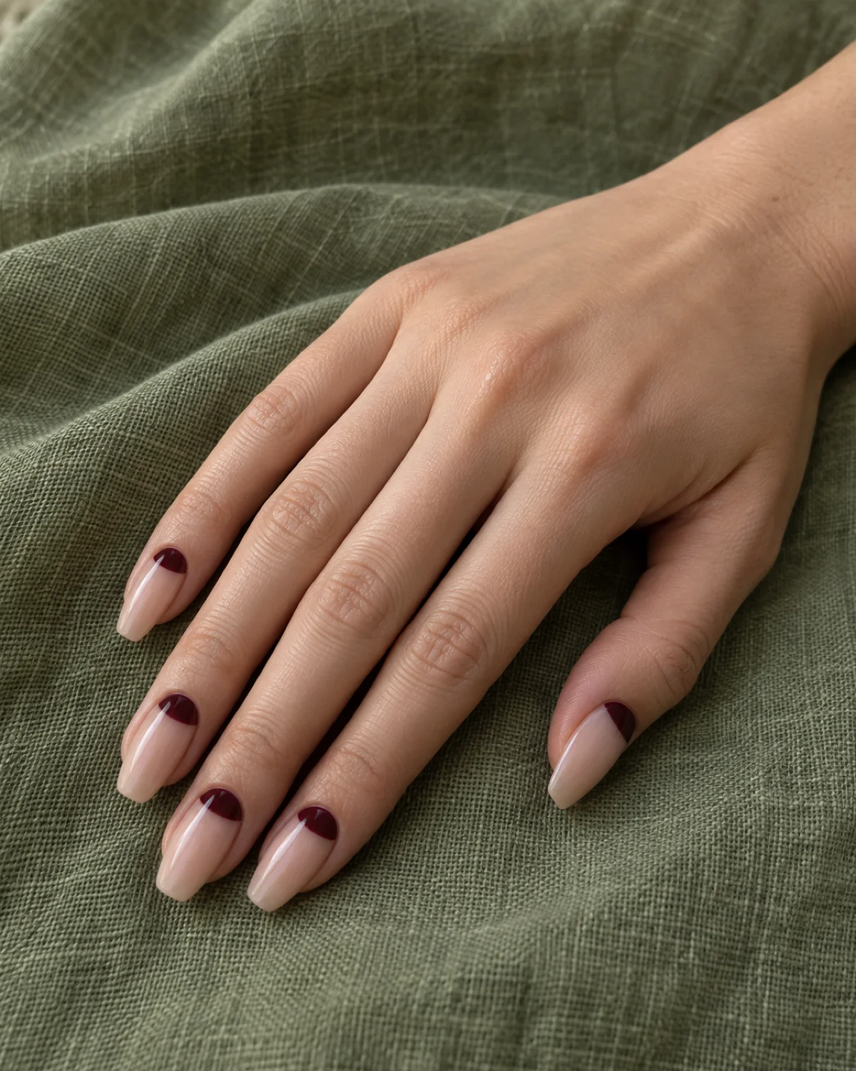 Single right hand with burgundy half-moon elegant nails on medium coffin shape resting on sage green linen