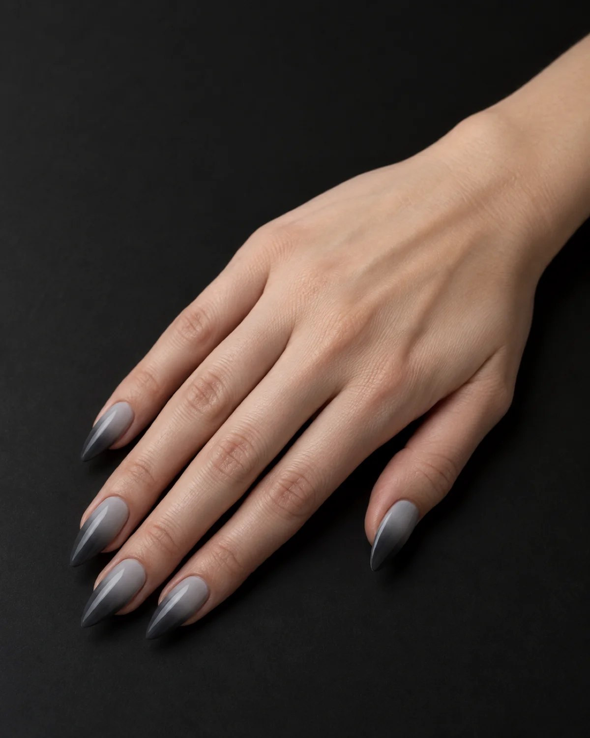 Single right hand with smoke grey gradient elegant nails on medium stiletto shape resting on matte black surface