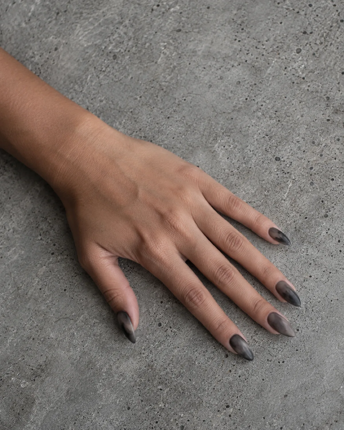 Smoky grey wash nails on almond shape with uneven charcoal watercolor effect on concrete slab