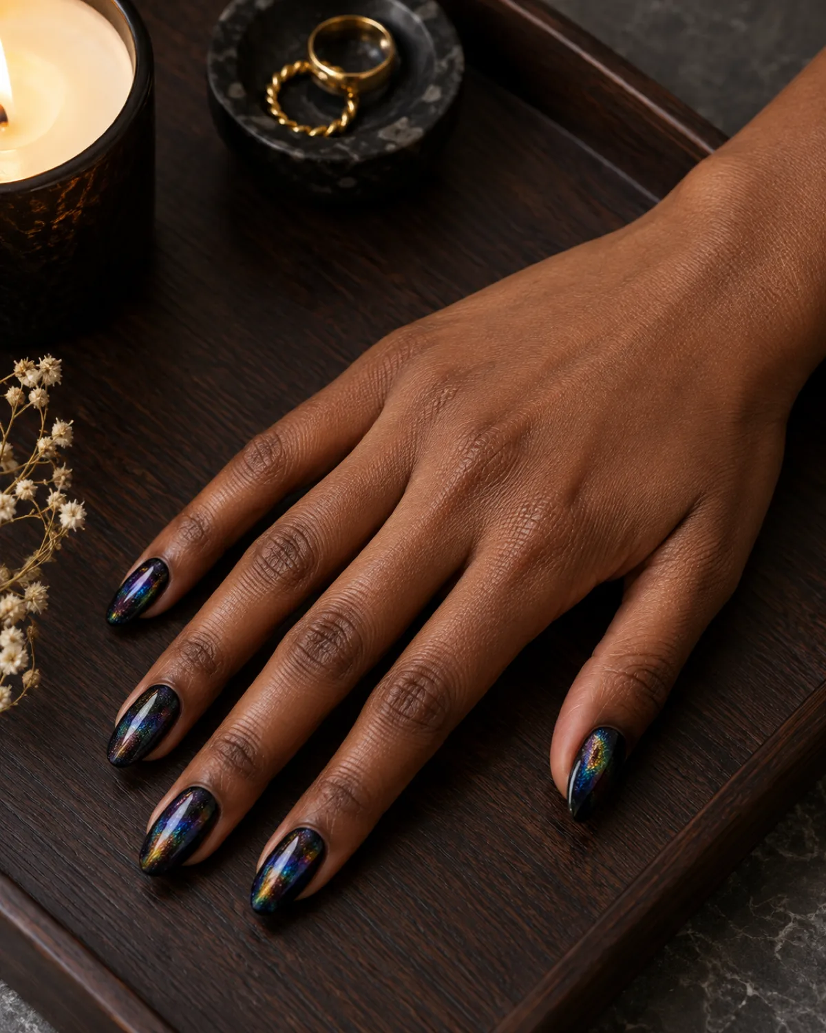 Dark holographic almond nails with rainbow shift on near-black base on dark wood tray