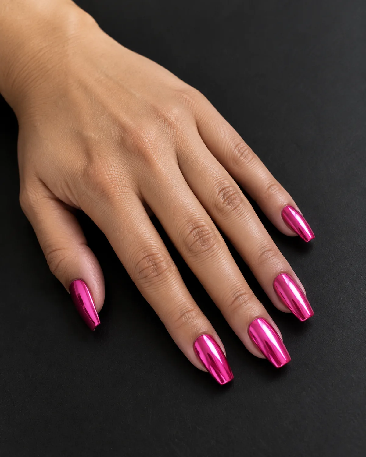Single left hand with hot pink chrome mirror nails on medium coffin shape resting on a matte black surface