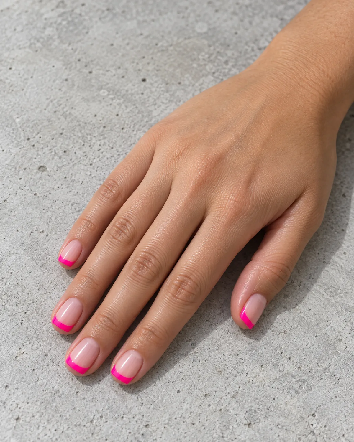 Single right hand with neon hot pink French tips on short square nails resting on a light grey concrete surface
