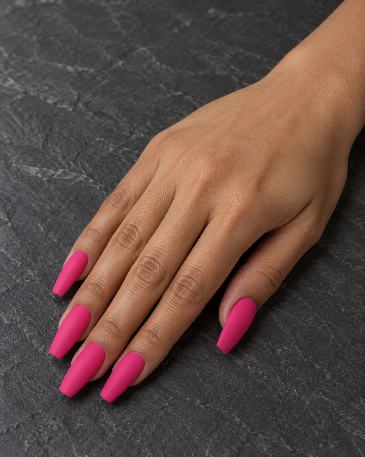 Single right hand with matte hot pink nails on long coffin shape resting on dark grey slate