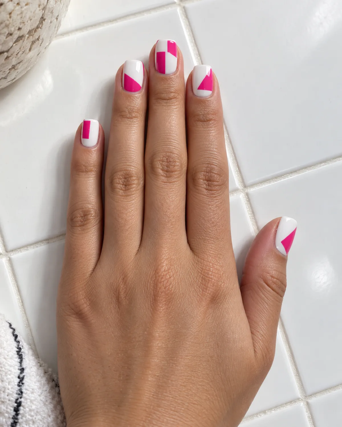 Single right hand with geometric hot pink blocks on white base on medium square nails resting on white ceramic tile