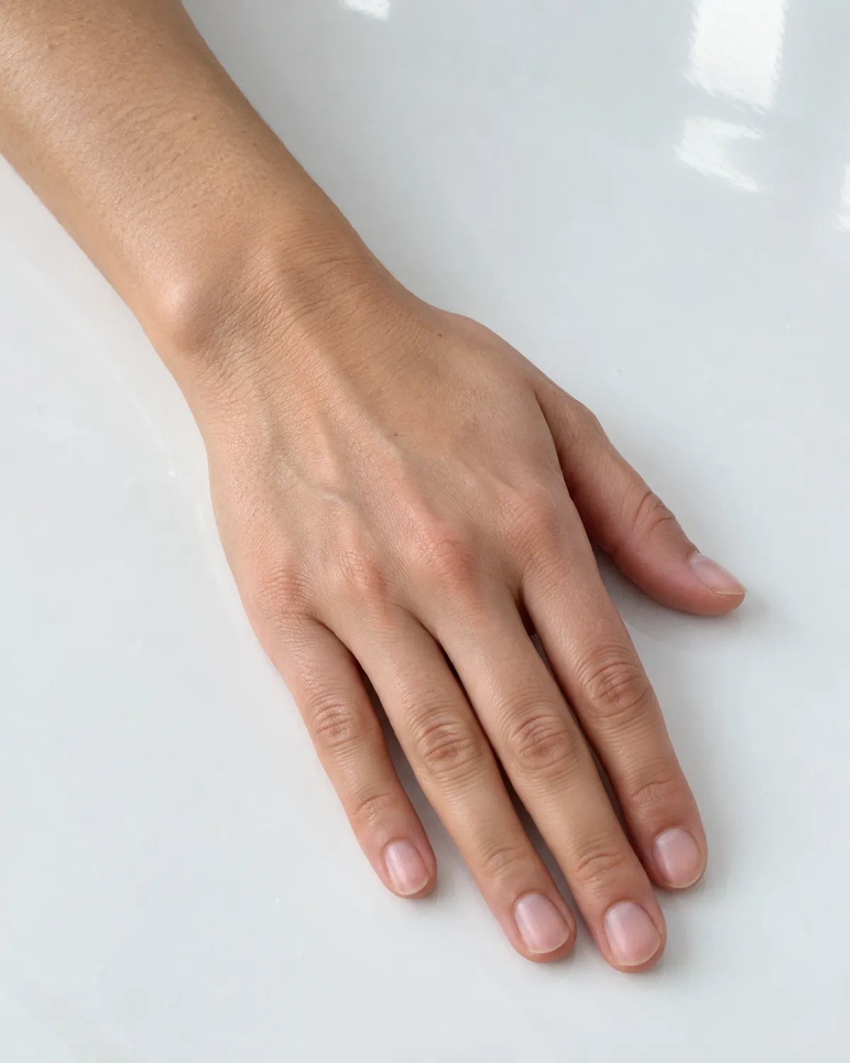 Left hand on white porcelain surface with short bare natural nails showing clean smooth texture after proper acrylic removal