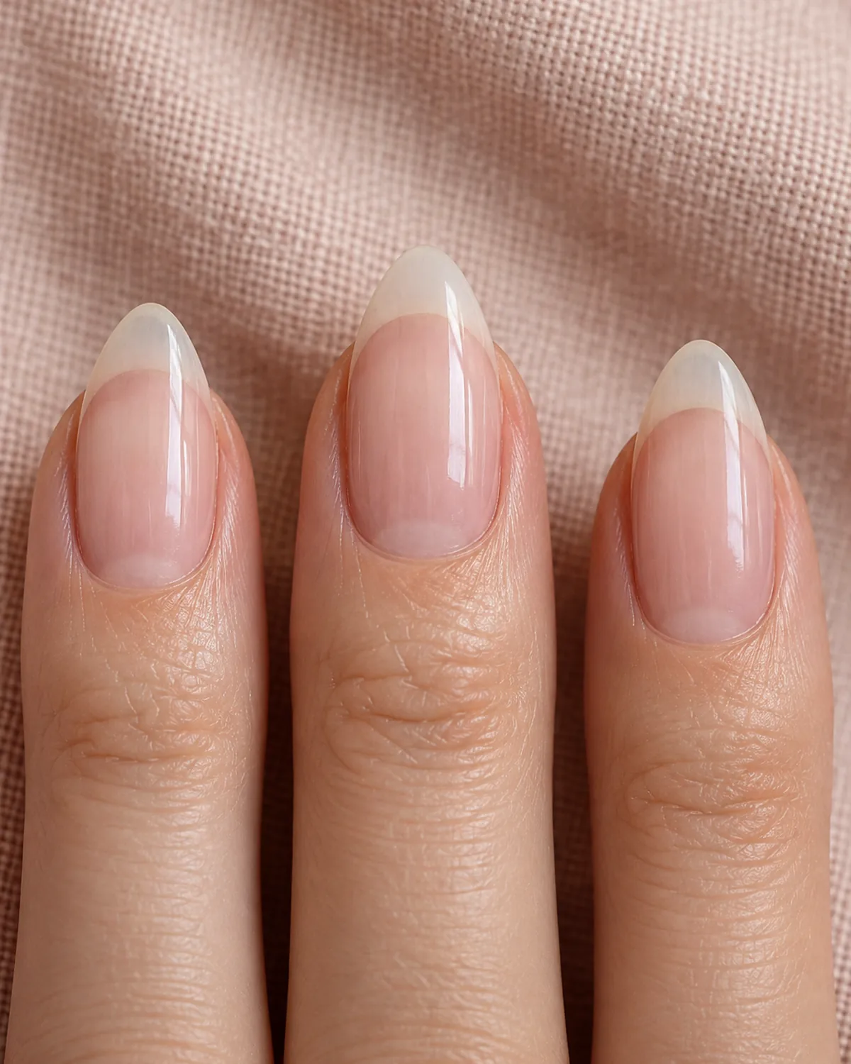 Close-up of three fingertips with freshly shaped almond nails, straight tapered sides meeting in a smooth softly rounded peak with a clear glossy coat