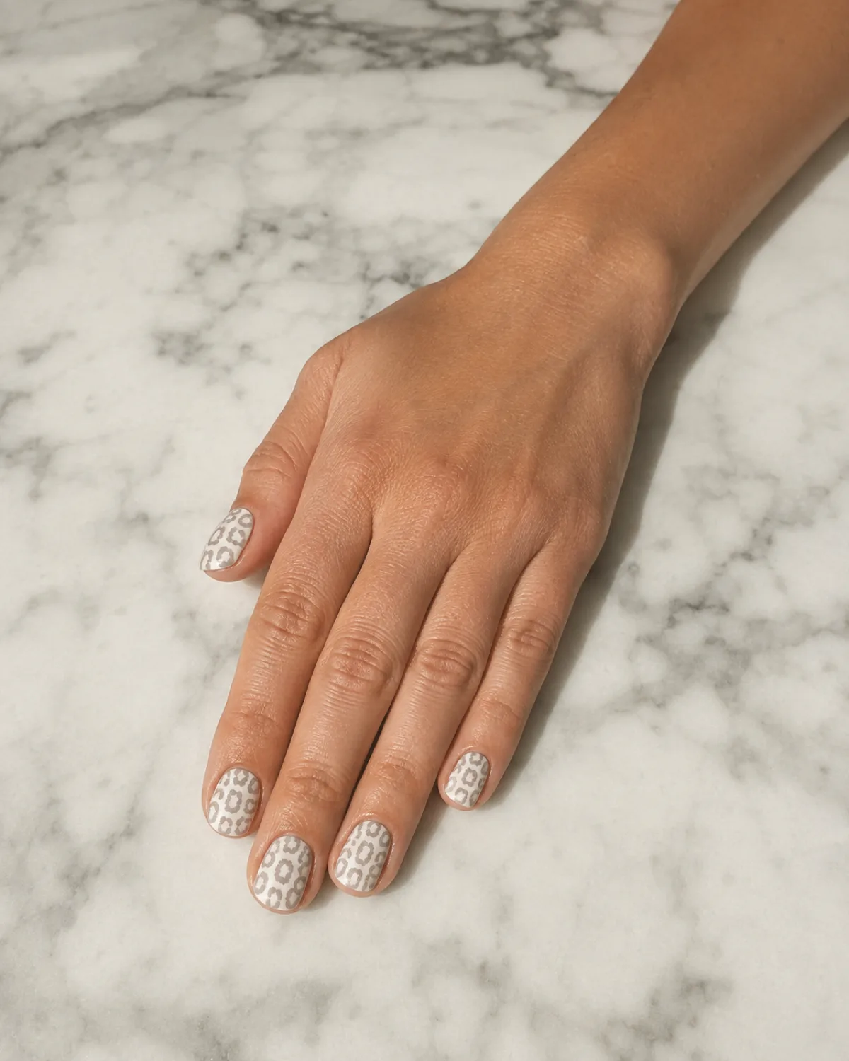 Single left hand with short oval nails in white leopard print resting on white marble