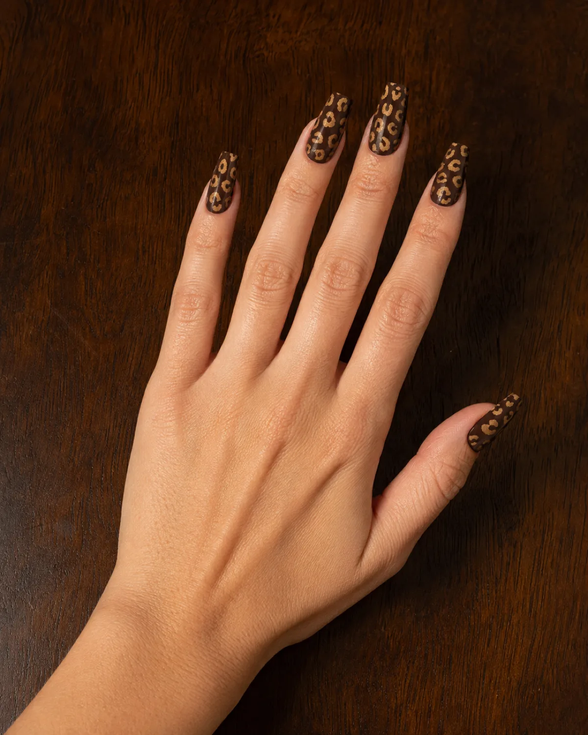 Single left hand with medium coffin nails in reverse leopard print on dark walnut table
