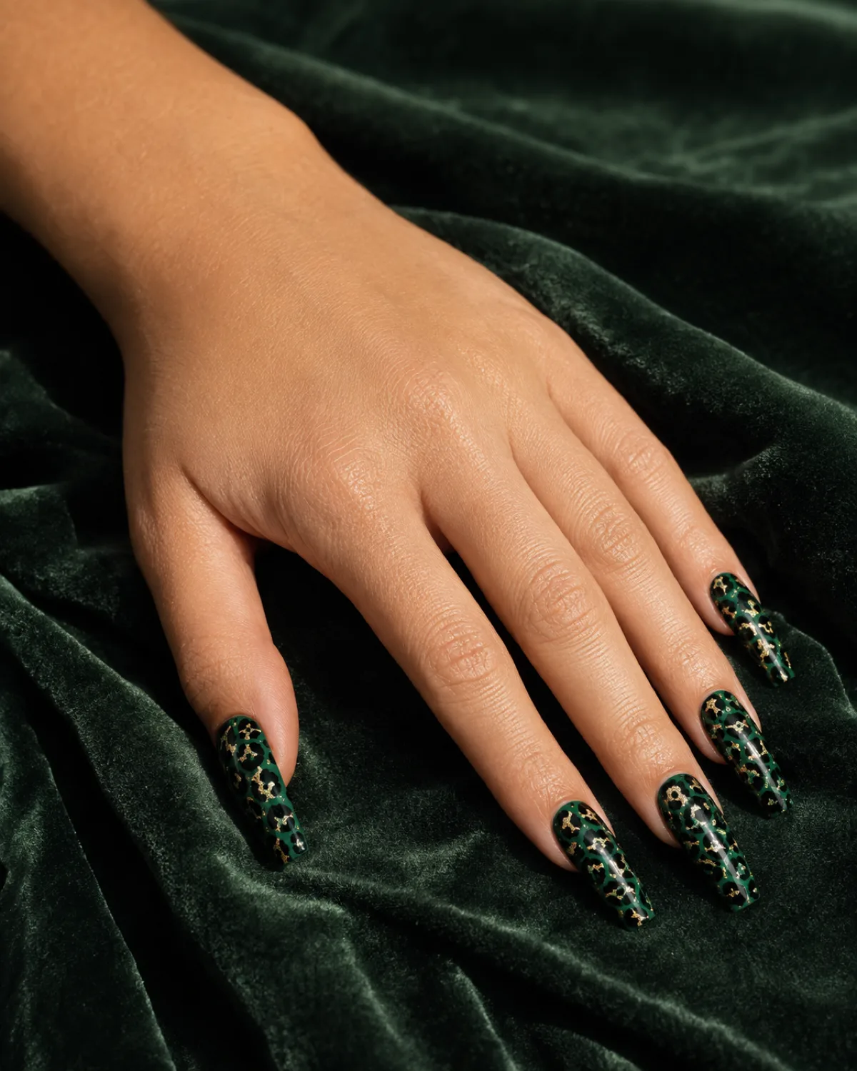 Single left hand with long coffin nails in emerald leopard print on dark green velvet