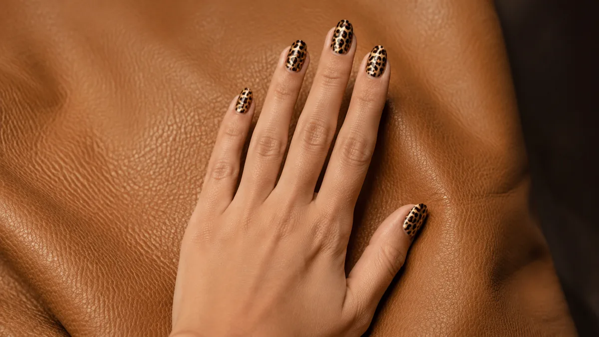 Single right hand with medium almond nails in classic golden leopard print resting palm down on camel leather