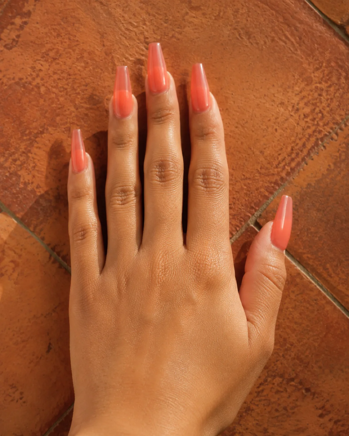 Single left hand with long coffin nails in warm coral jelly finish resting palm down on terracotta tile