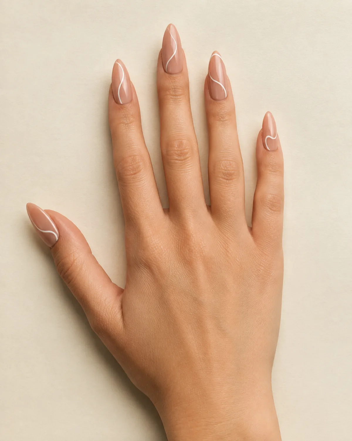 Single right hand with long almond nails showing warm nude base with thin white curved line art resting palm down on cream paper