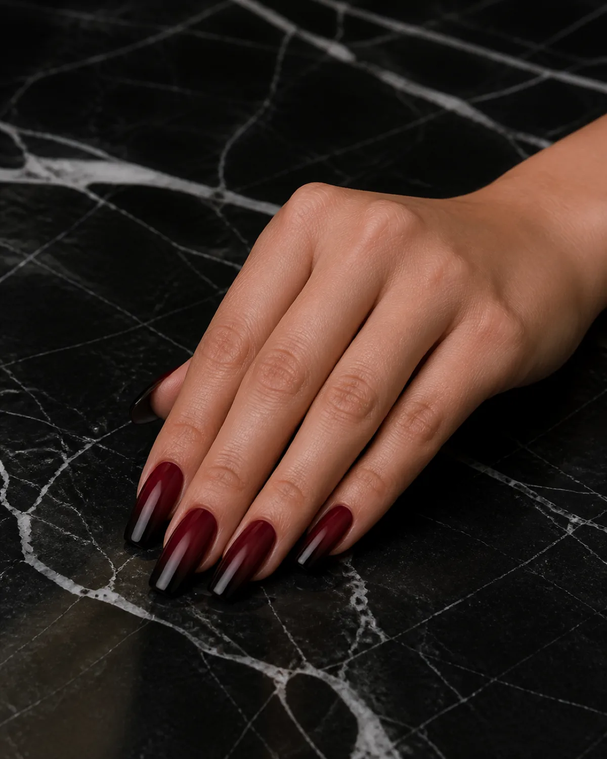 Single right hand with medium coffin nails showing burgundy to near-black ombre gradient resting on black marble with fingers together