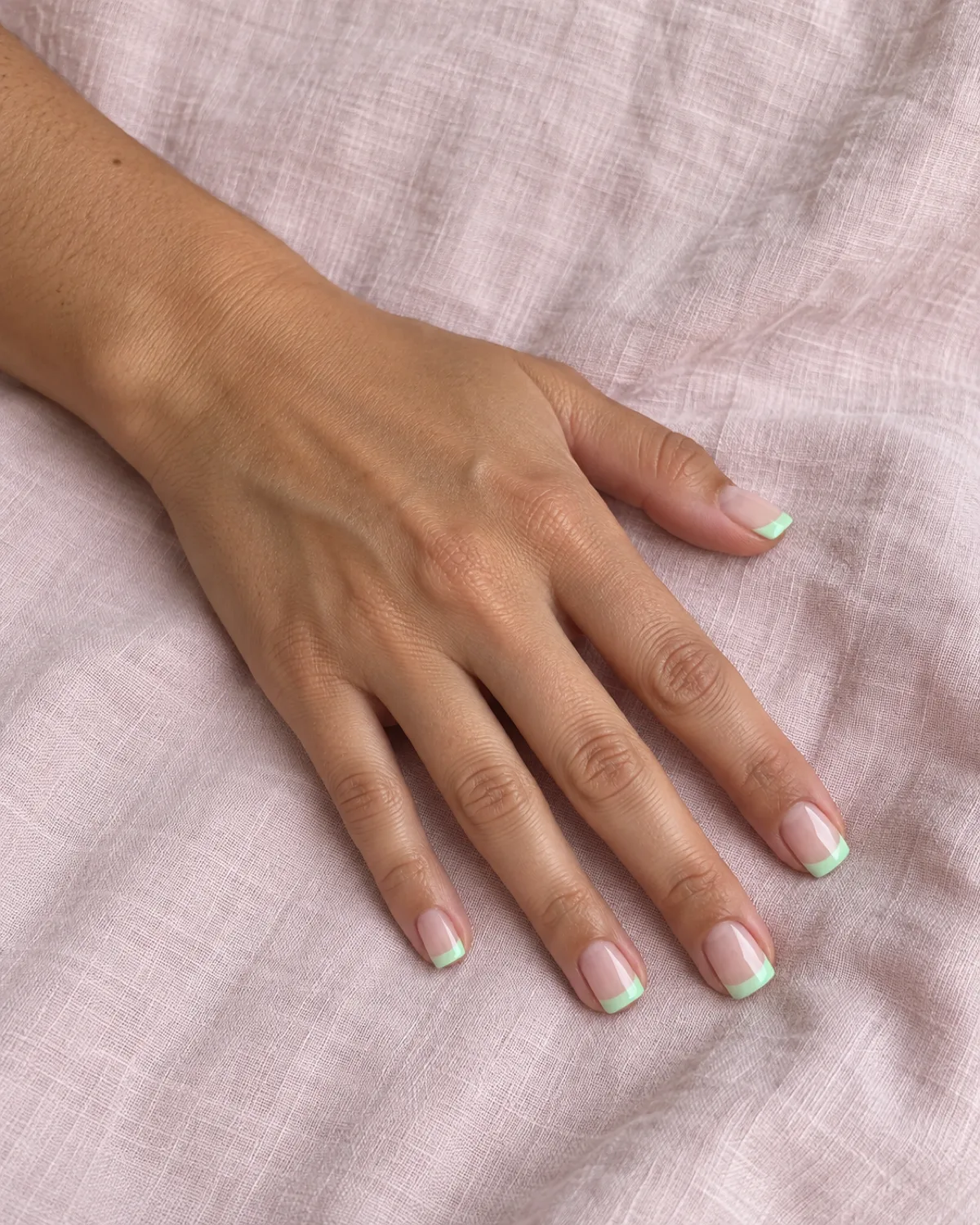 Mint green French tip nails on short square shape with nude base on pale pink linen