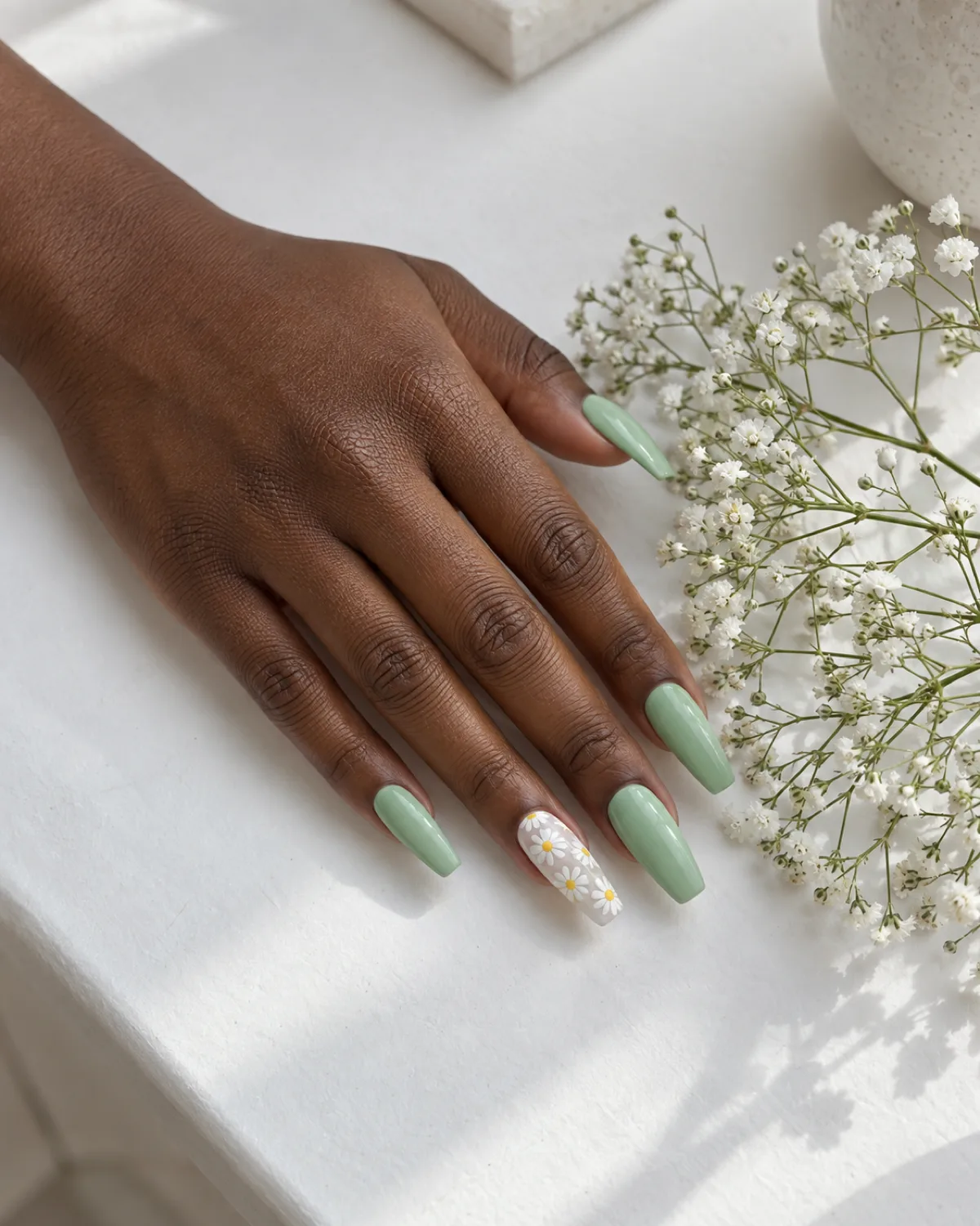 Mint green nails with white daisy accent on ring finger coffin shape alongside baby's breath