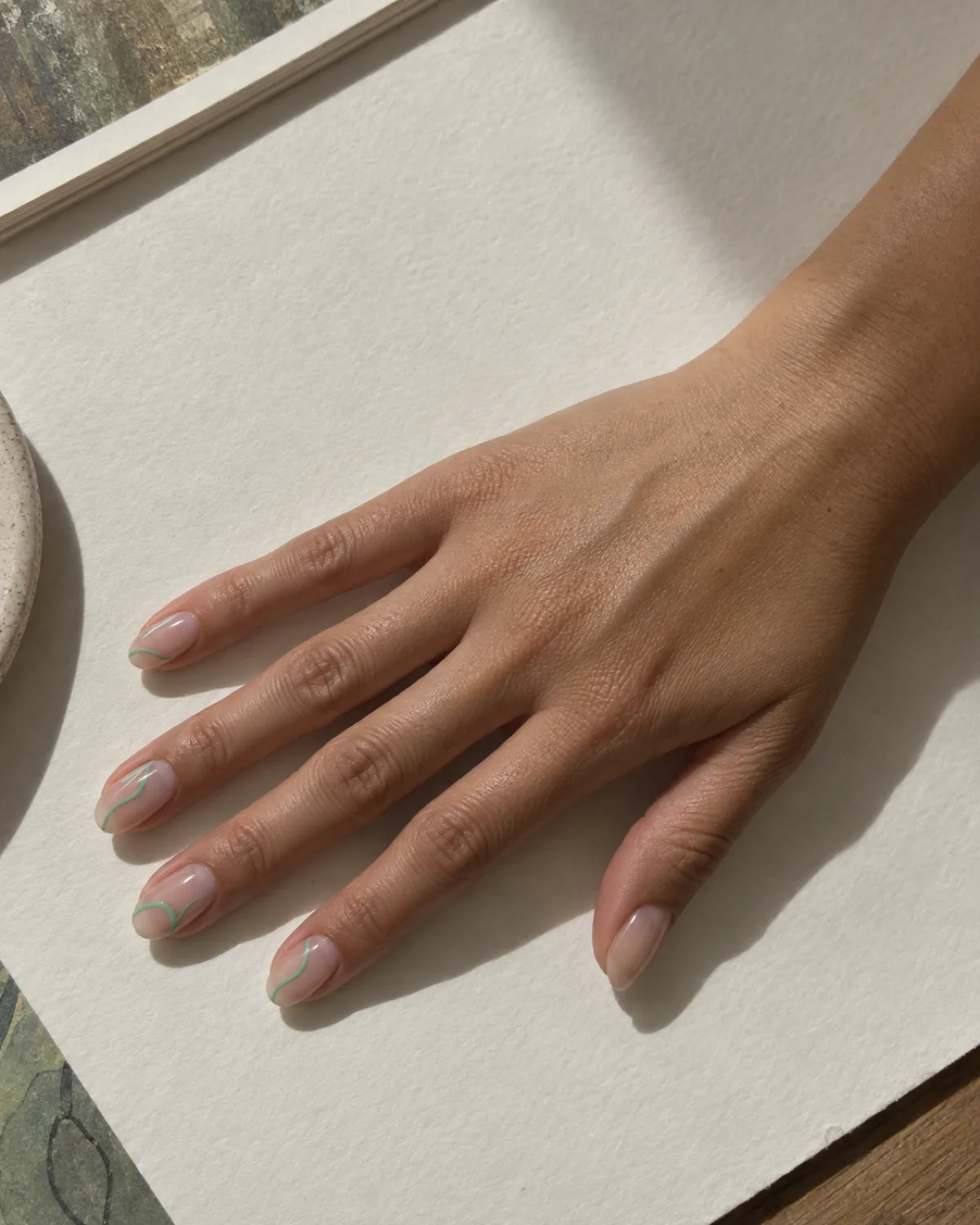 Mint green abstract line art on nude oval nails on off-white drawing paper