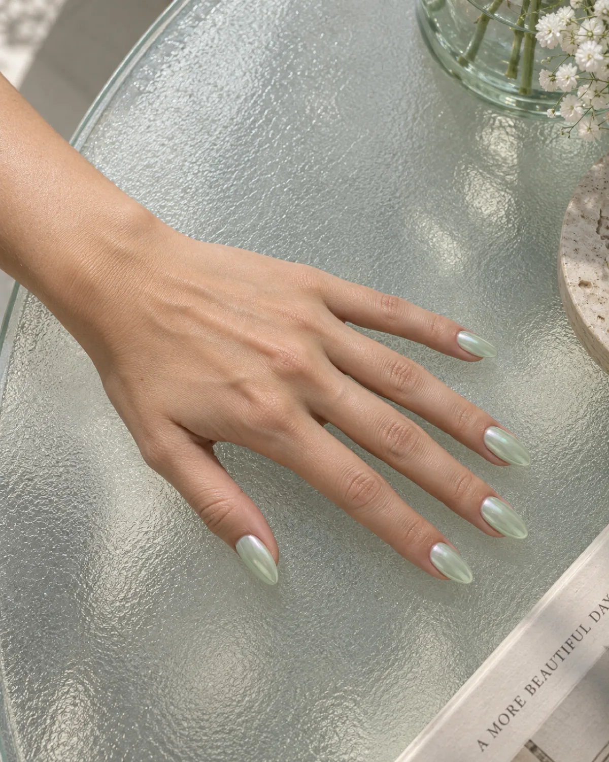Mint green glazed donut nails with pearlescent shimmer on almond shape on frosted glass
