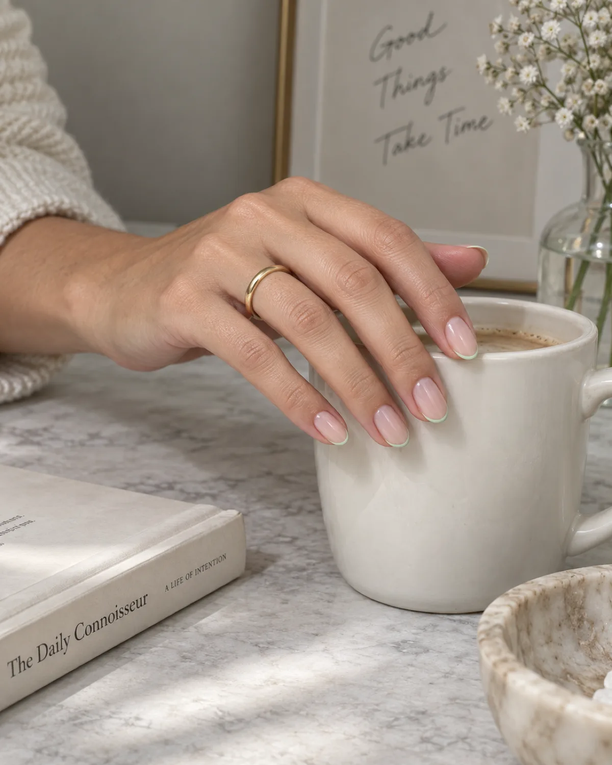 Mint green micro French tip line on almond nails resting on white ceramic mug edge