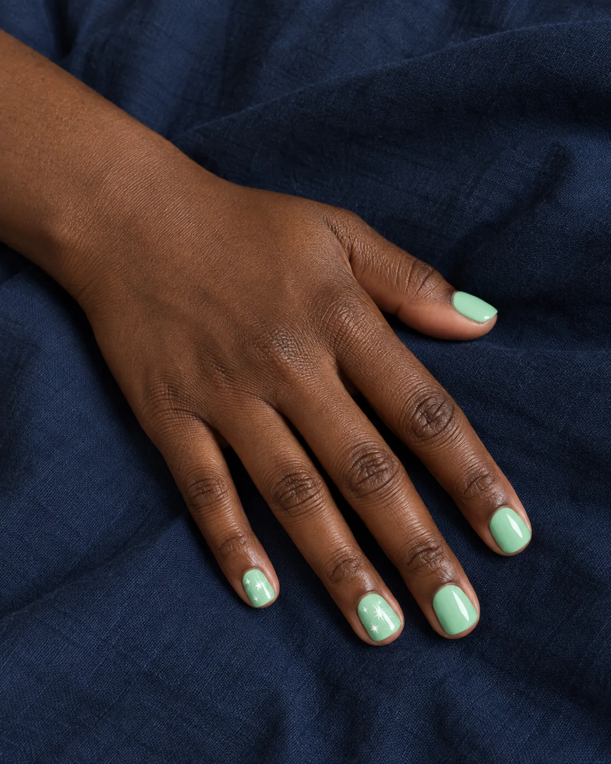 Mint green nails with white star stamps on short square shape on dark navy fabric