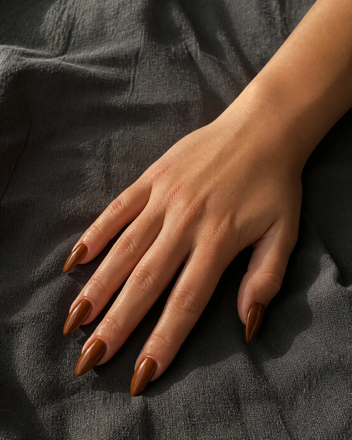 Single right hand with medium stiletto nails in toffee glaze resting palm down on charcoal linen