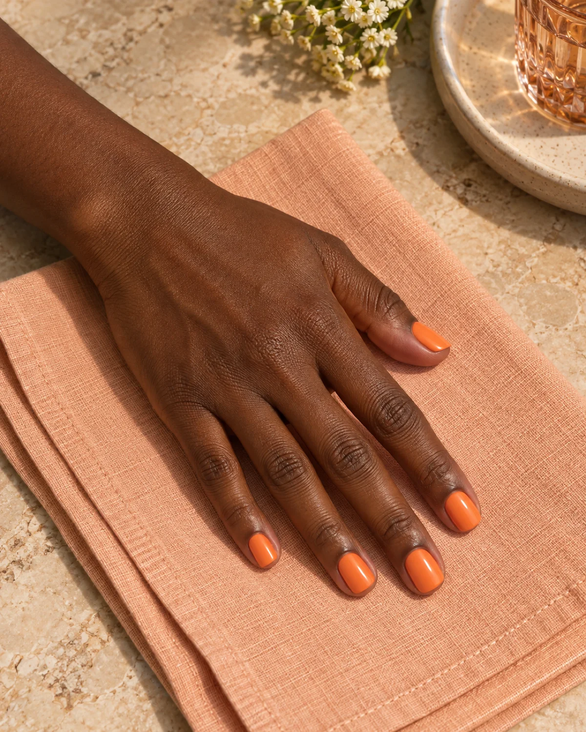 Single left hand with glossy apricot short square nails on a folded peach linen napkin
