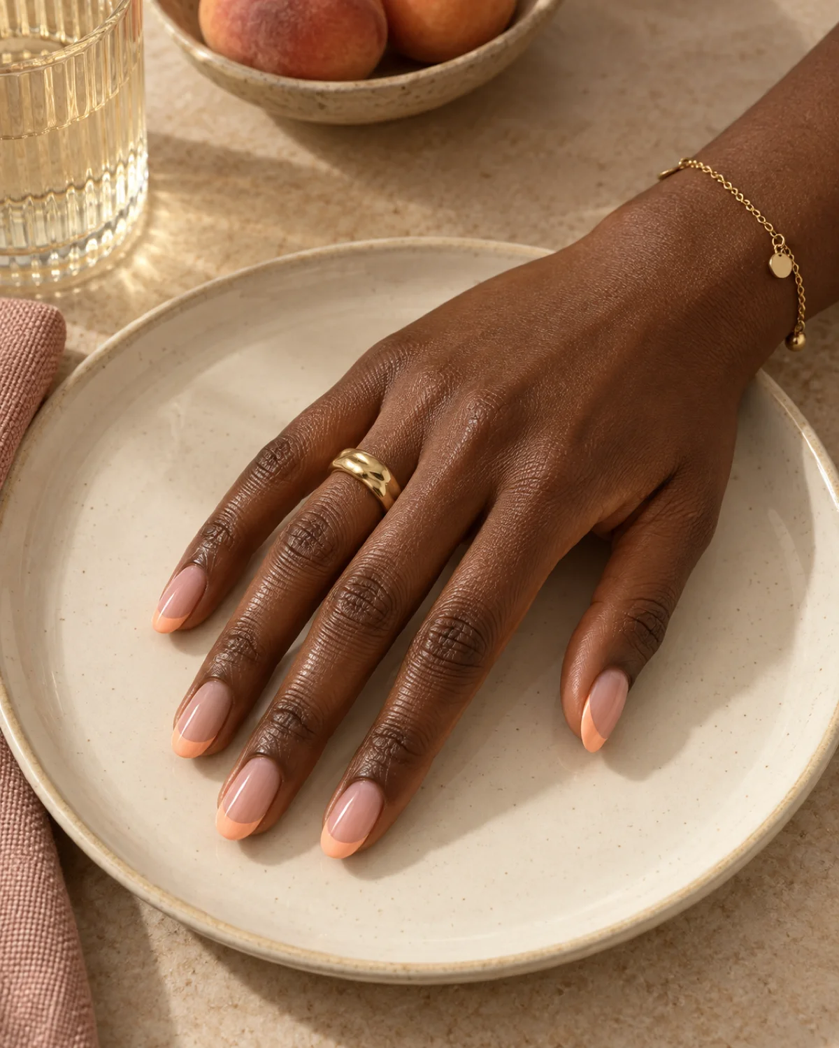 Single right hand with peach French tip round nails on a cream ceramic plate