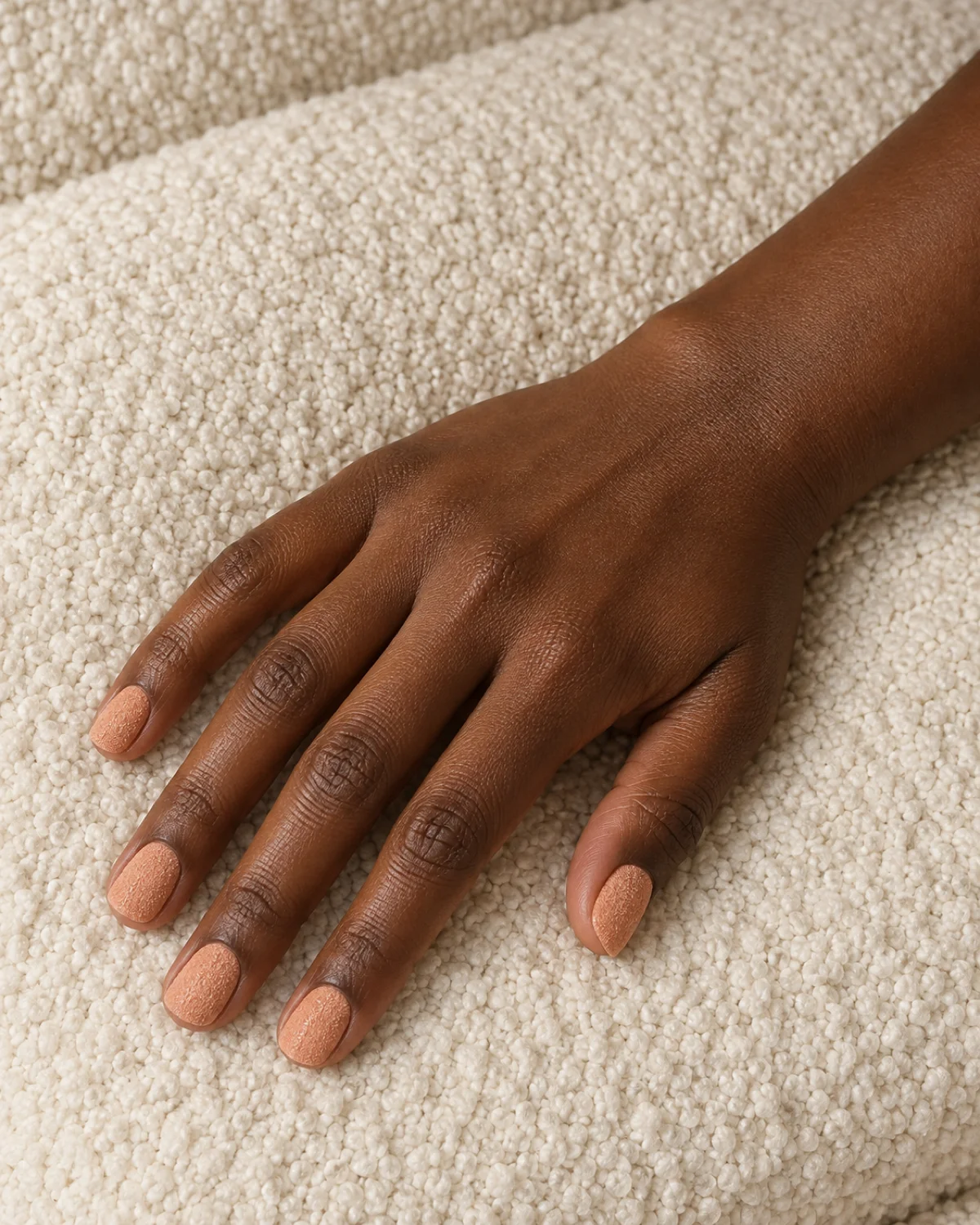 Single right hand with peach sugar-texture short natural nails on cream bouclé fabric