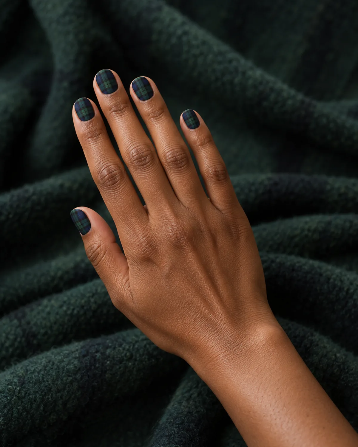 Raised hand with Black Watch tartan nails in navy, bottle green and black with a velvet no-shine finish on short round shape
