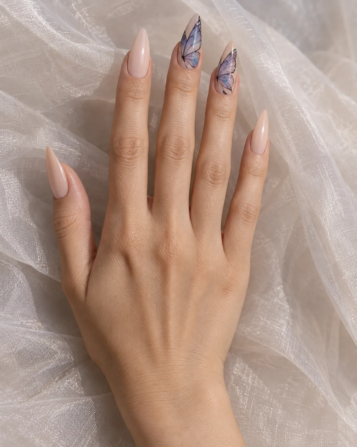 Single right hand with stiletto nails and butterfly wing art on ring and middle finger resting palm down on sheer organza fabric