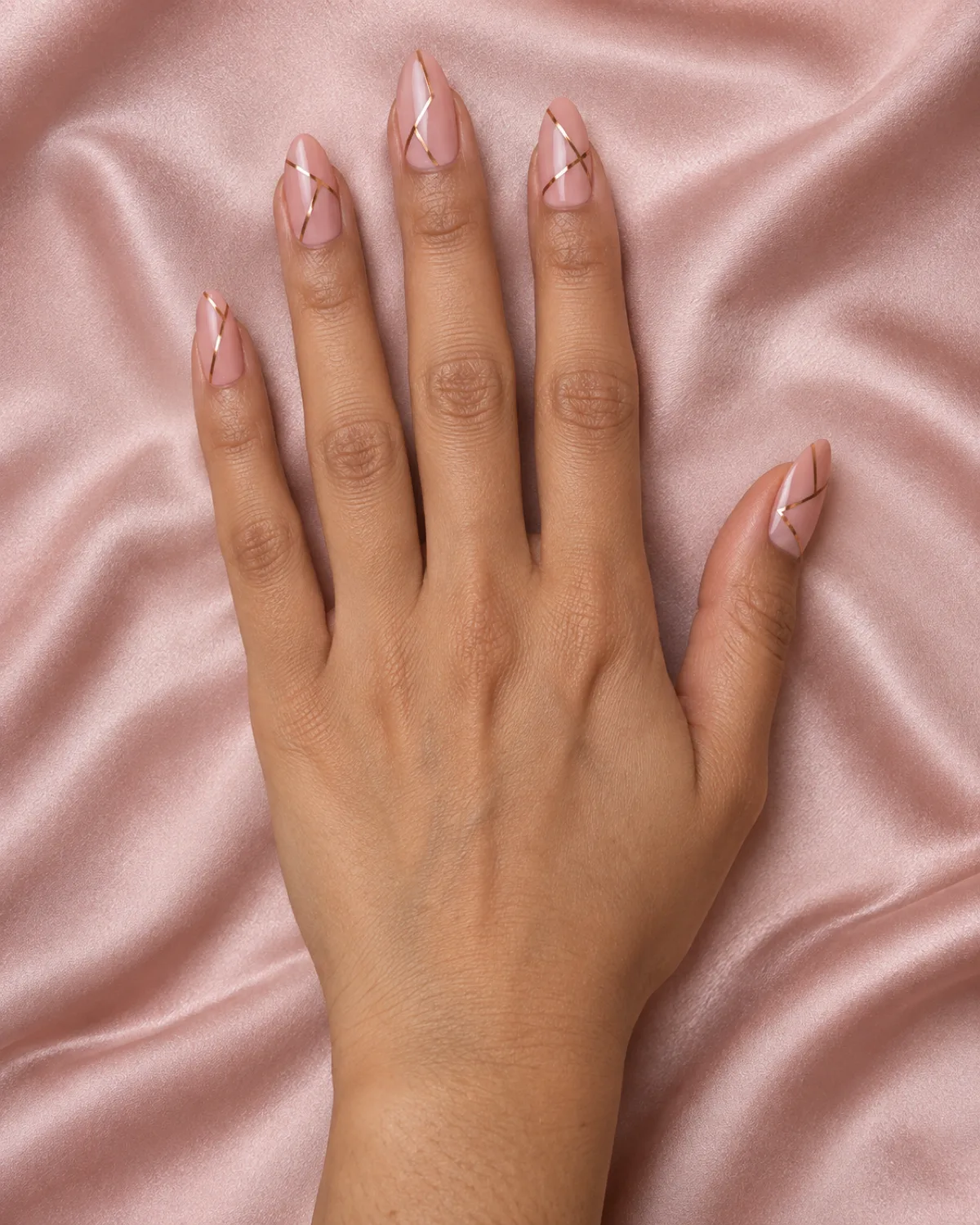 Single right hand with almond nails showing geometric rose gold line design on blush pink satin fabric